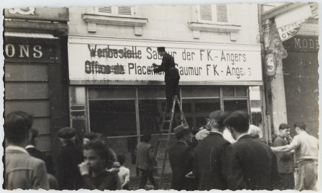 Agent de police recouvrant de peinture l'enseigne de l'Office de placement allemand, rue d'Orléans à Saumur, août 1944